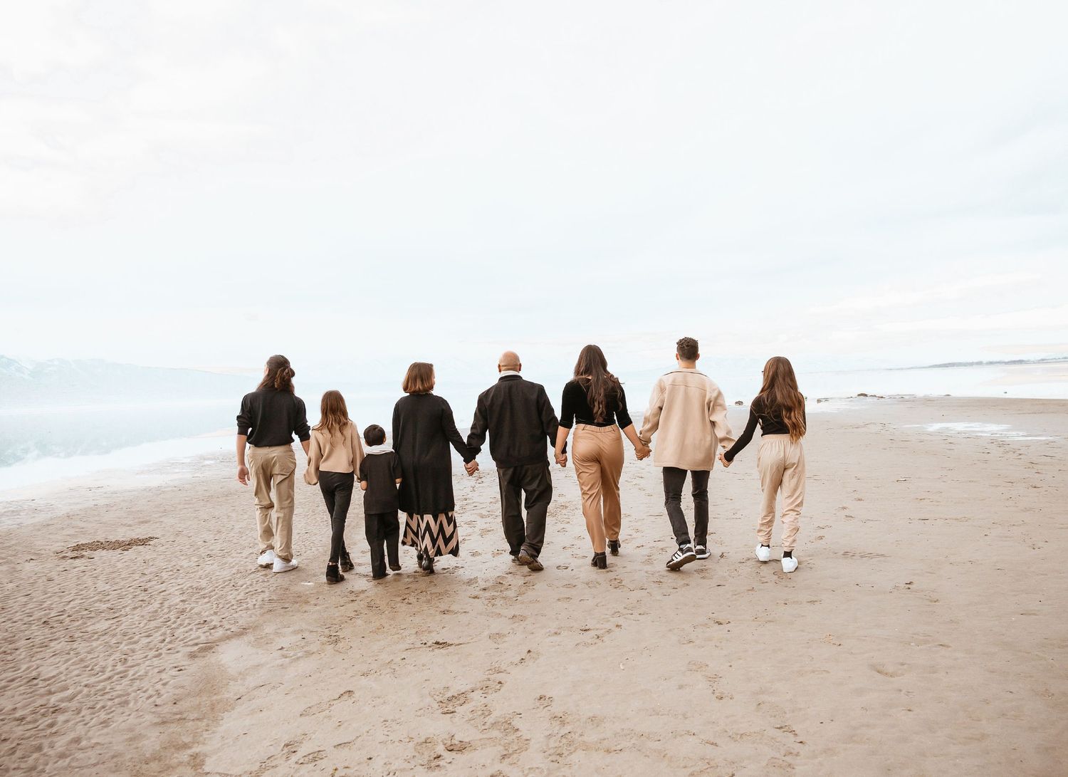 Group of people walking together along a sandy beach shoreline at sunset.