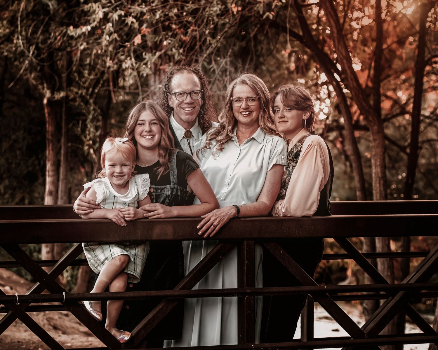 Family photo session in autumn forest with warm lighting and rustic wooden bridge setting.