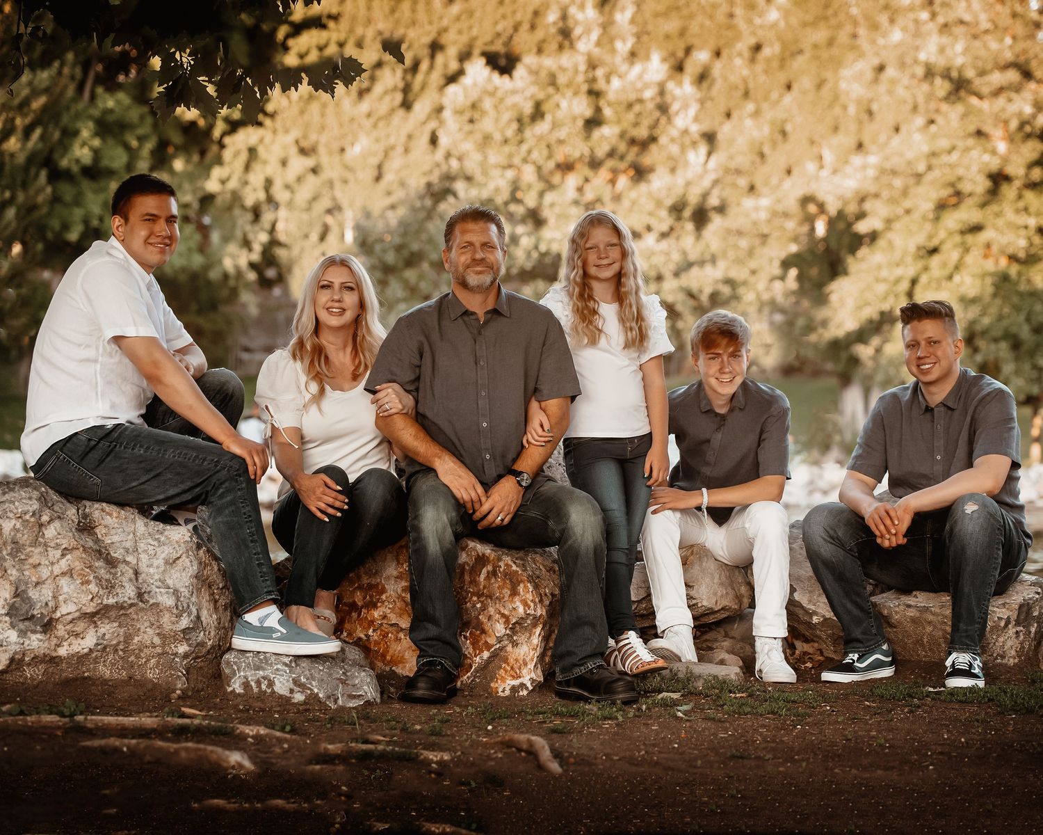 A group of people in casual attire sit together on large rocks during golden hour at sunset.