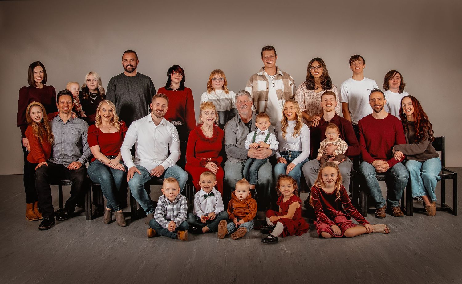 Large family portrait with multiple generations wearing coordinated red and white outfits seated together in a studio setting.