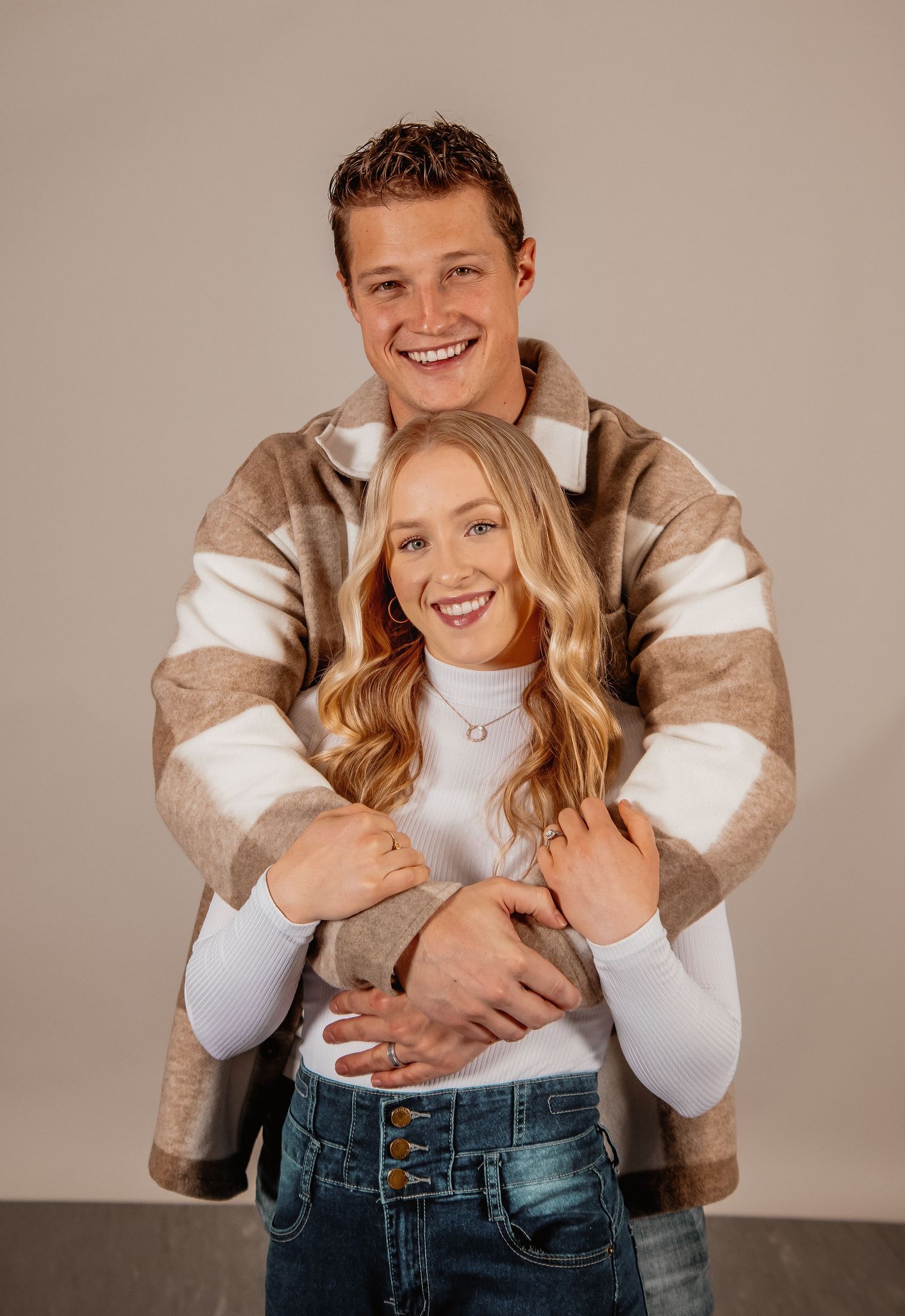 A couple in coordinating white and beige outfits pose together in a series of playful studio portraits.
