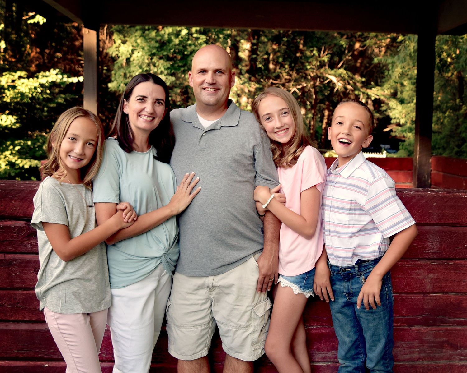 A series of outdoor family photos taken against a red wooden fence in a garden setting.