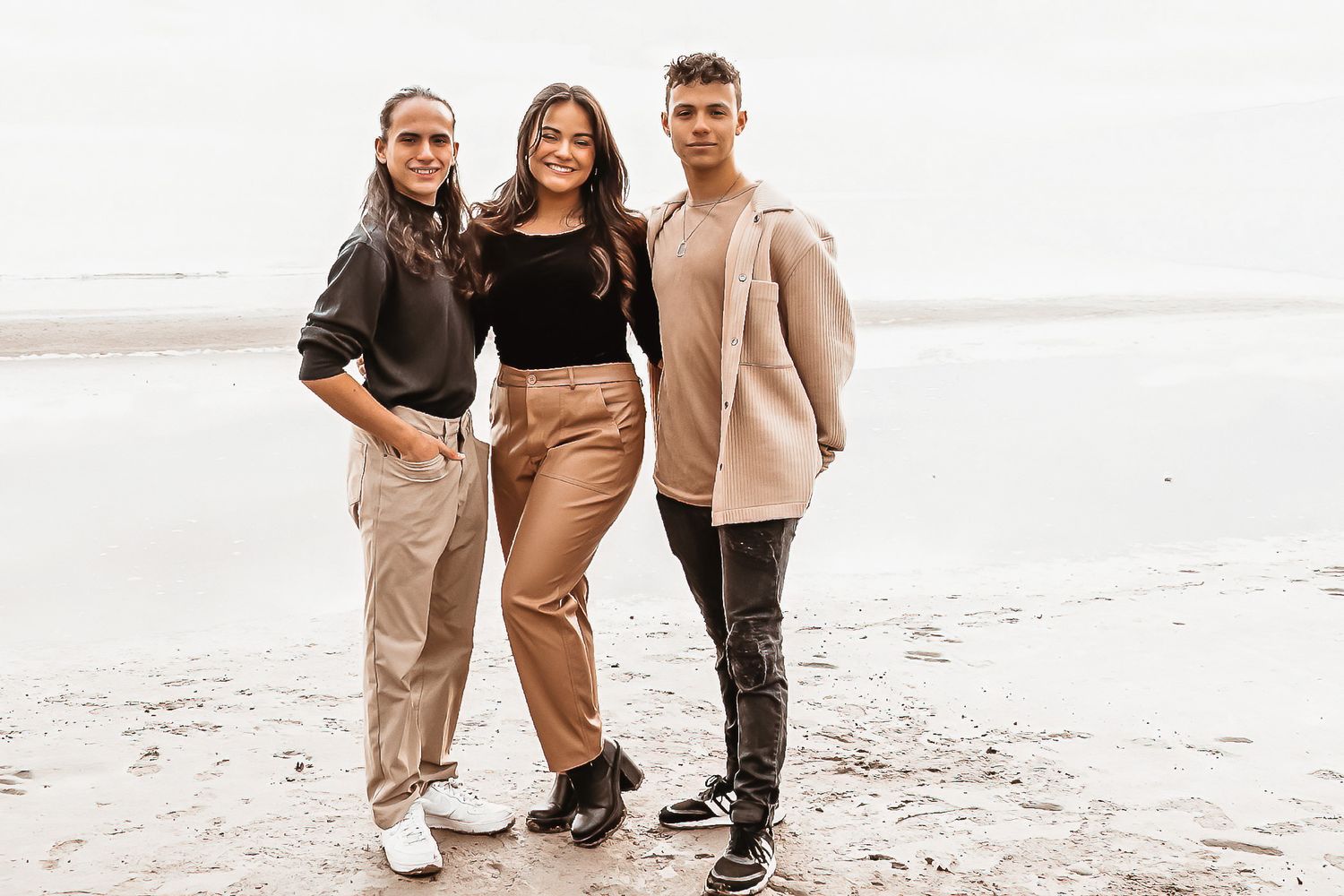 A family in neutral toned outfits poses together on a misty beach during a photo session.