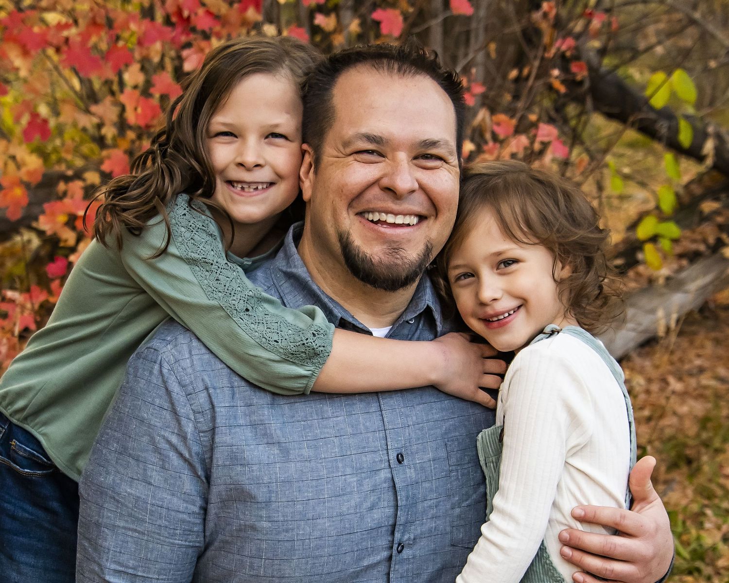 A series of candid outdoor family portraits captured against vibrant red autumn foliage in a park setting.