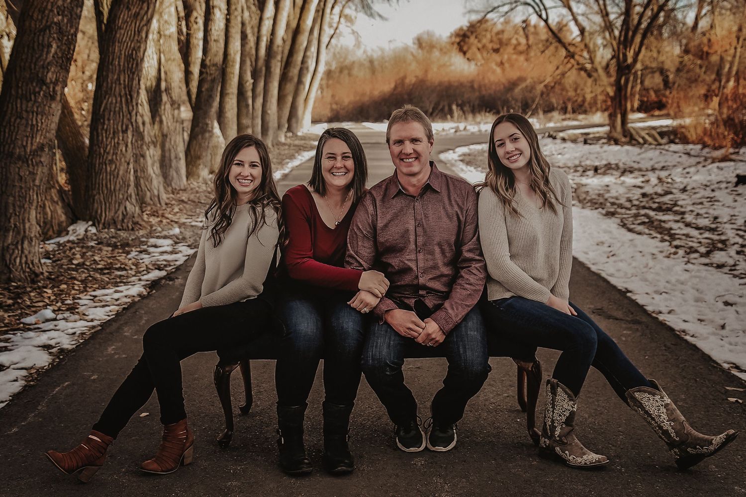 Family sitting together on wooden boardwalk in autumn forest setting during outdoor photo session.