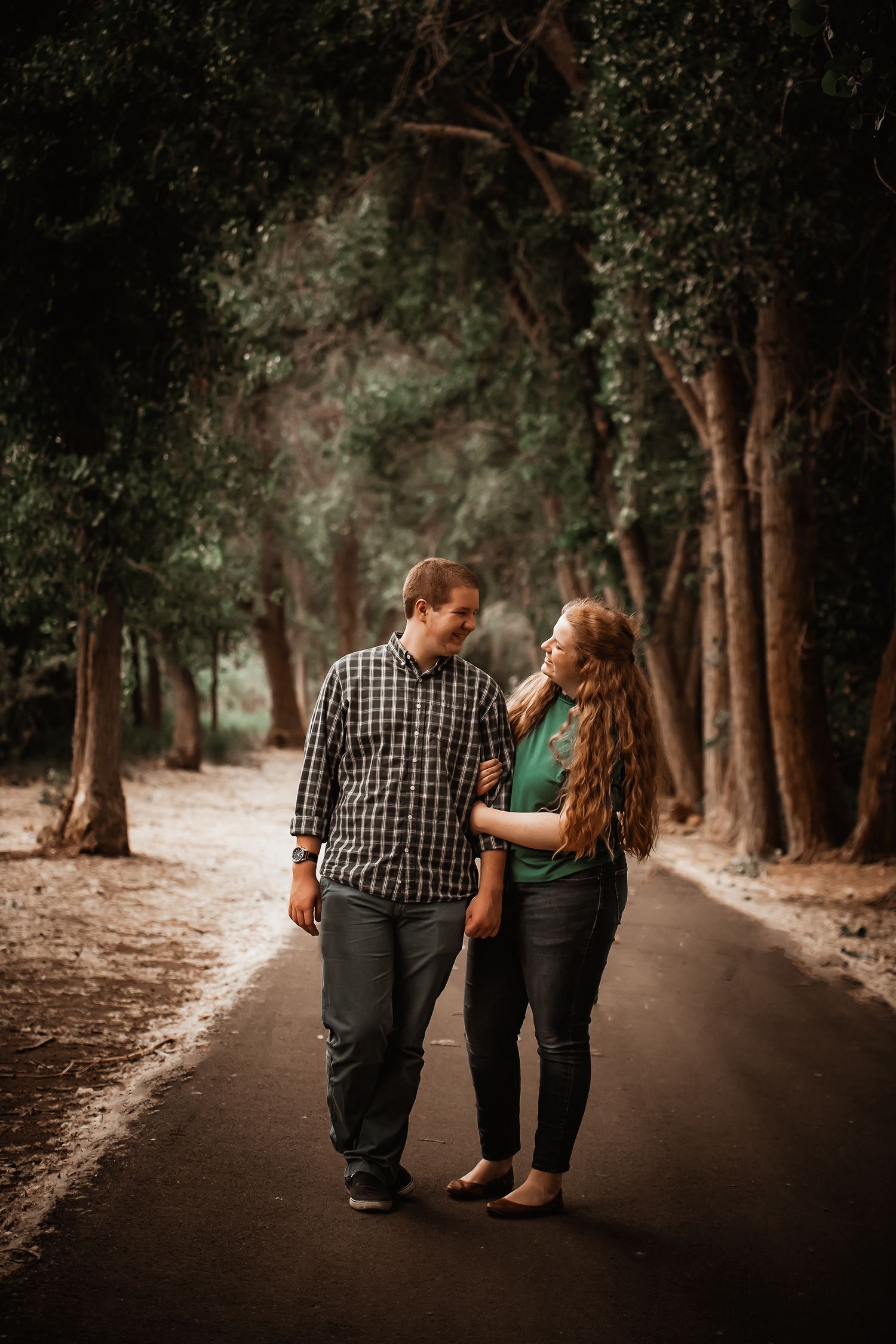 A couple walking together on a tree-lined path in a romantic outdoor setting during golden hour.