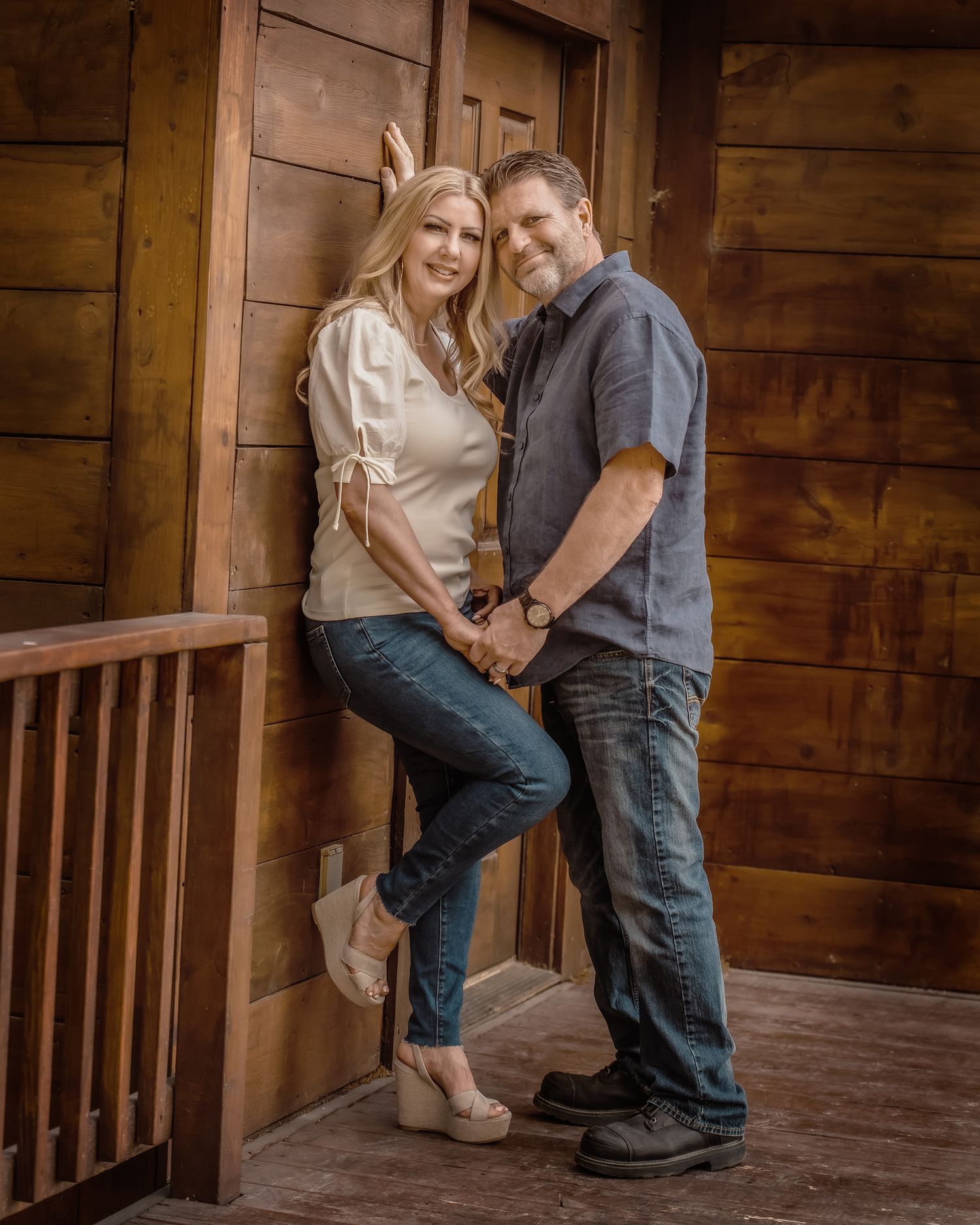 A romantic couple shares an intimate moment on a rustic wooden porch with warm lighting and natural wood surroundings.