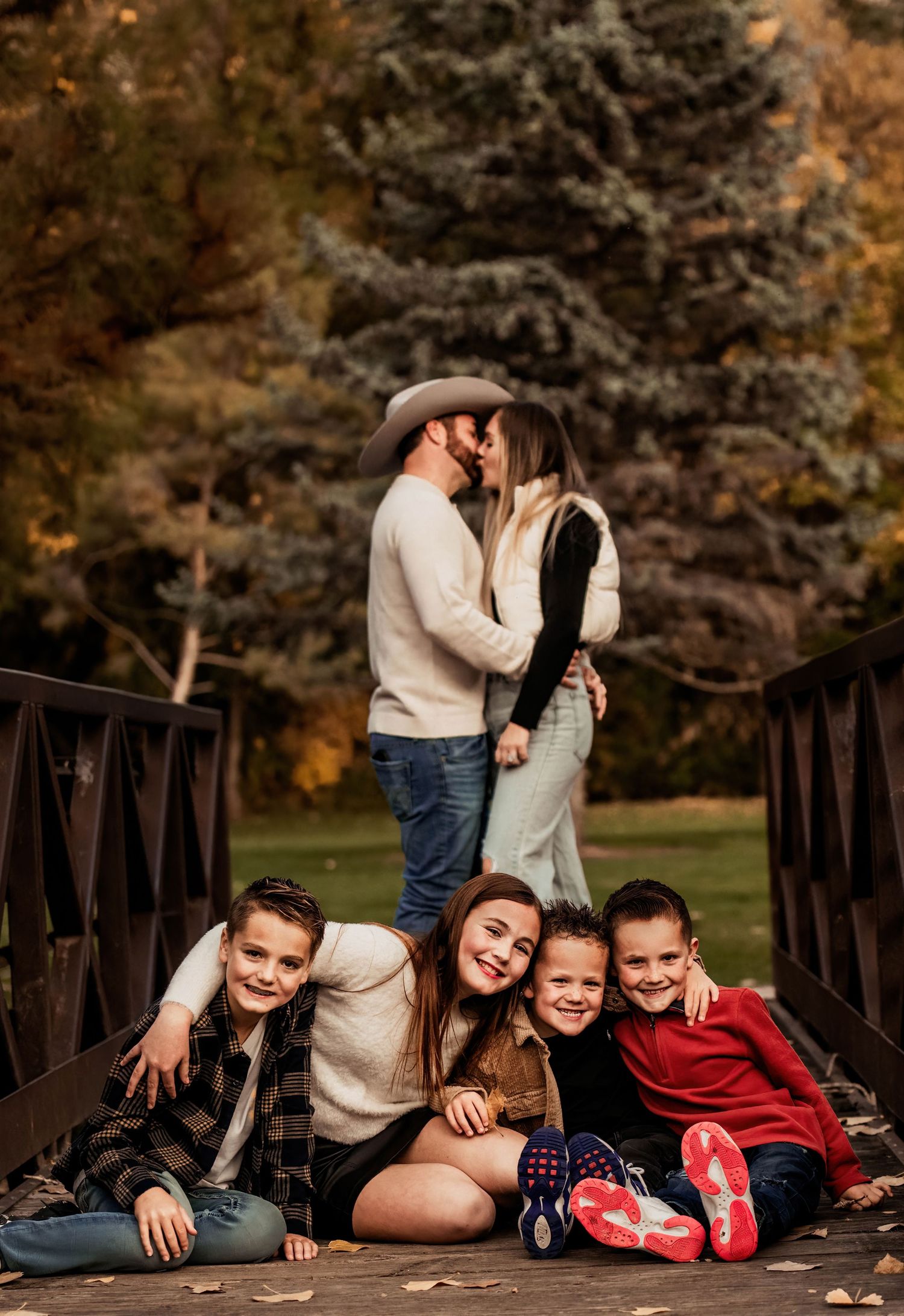 Family members share joyful moments together while posing on a wooden bridge during an autumn photoshoot.