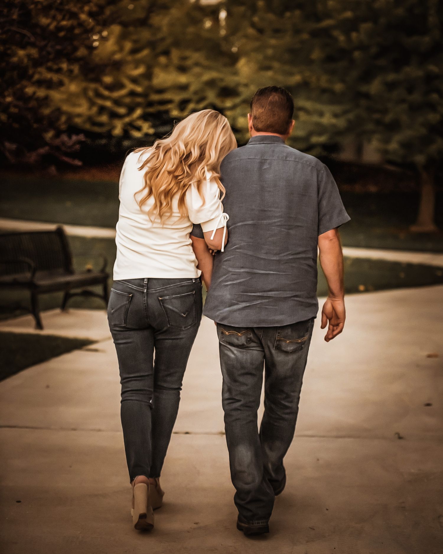 A couple walking together on a path wearing matching dark jeans and holding hands in a romantic outdoor setting.