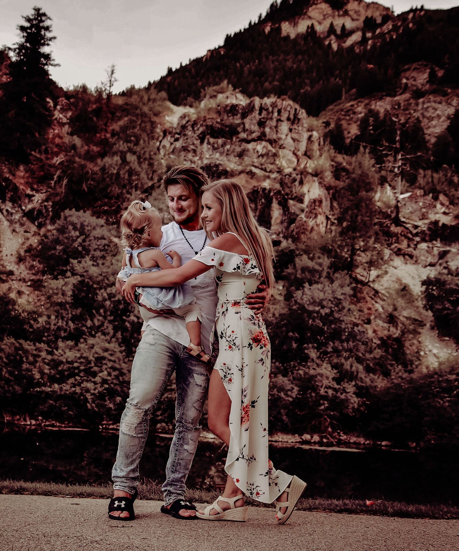 A couple embraces in a romantic moment against a scenic mountain backdrop during an outdoor photoshoot.