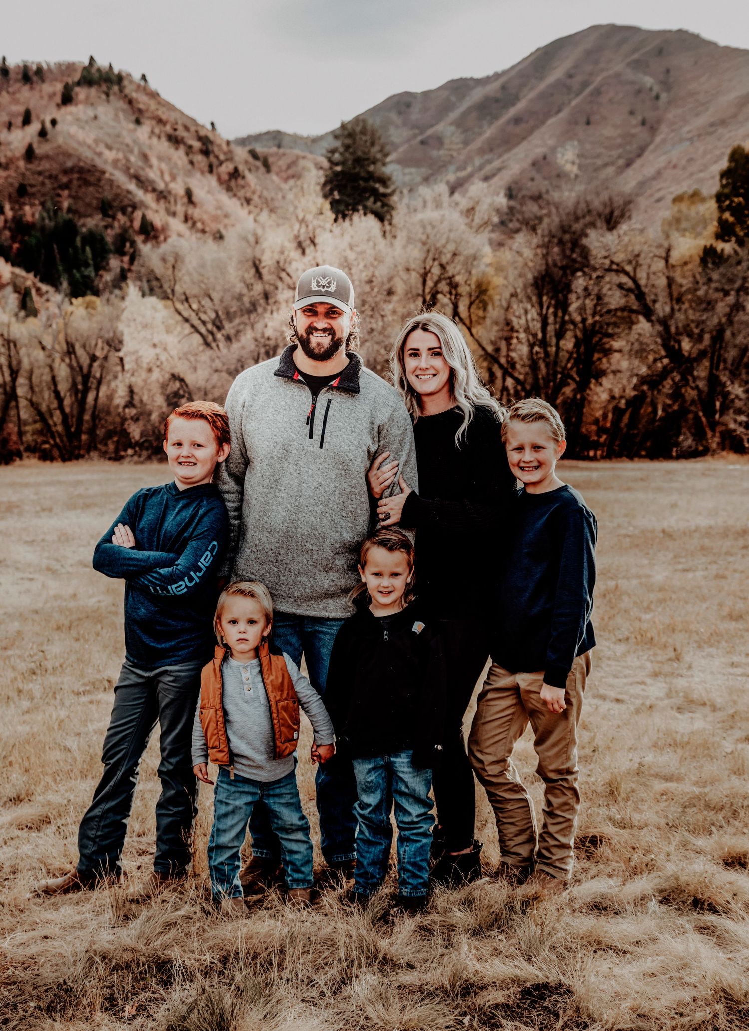 Family enjoying autumn day in mountain meadow with rugged peaks and fall foliage in background.