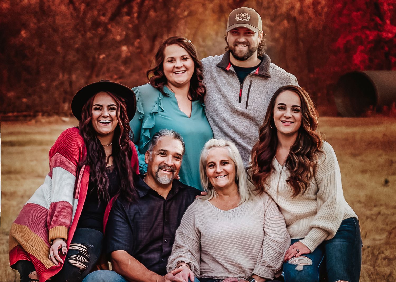 Family portrait session in a park with warm autumn colors and red foliage in the background.
