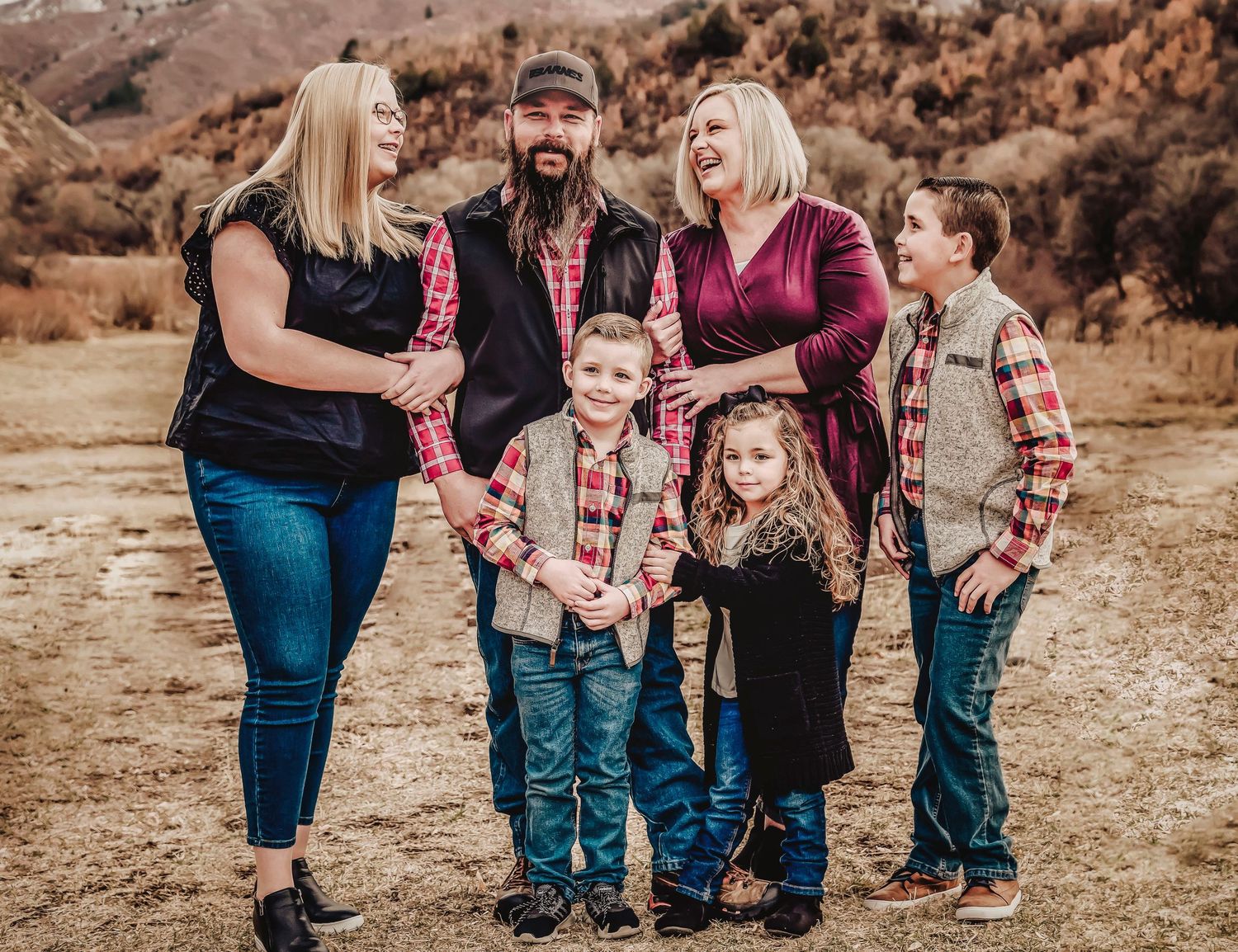 A family group poses together outdoors in coordinated casual outfits against a natural desert landscape backdrop.