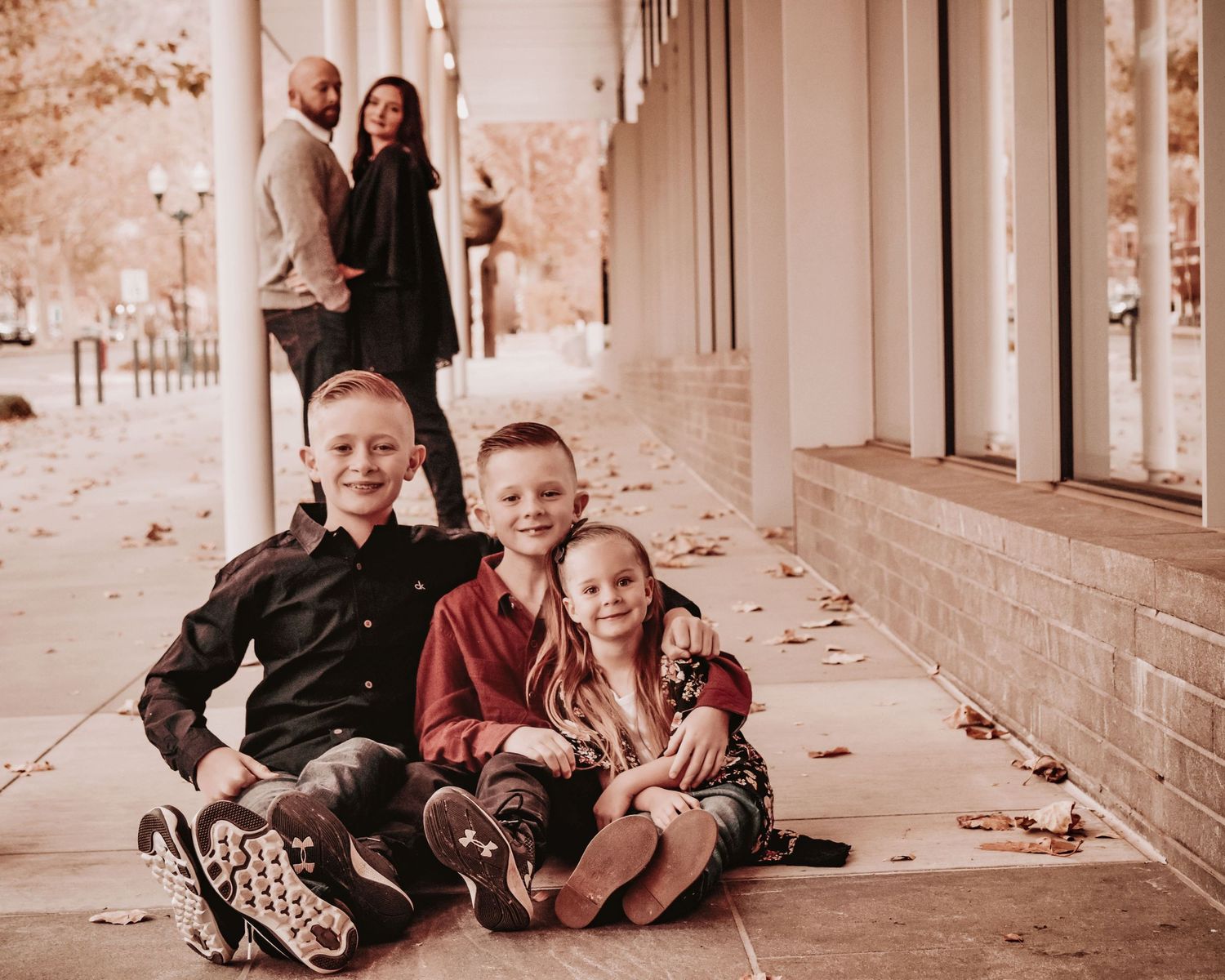 A family sits together on a rustic covered porch with vintage brick walls in sepia tones.
