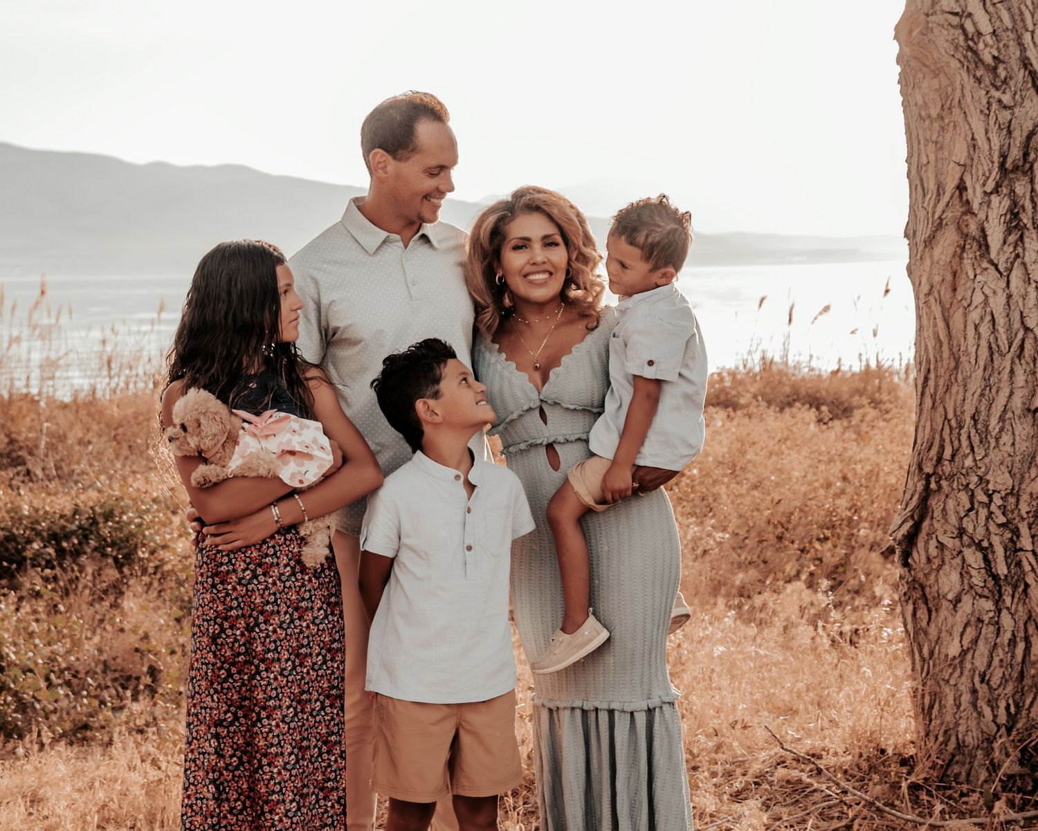 Family group in neutral colored outfits poses together in natural sepia-toned outdoor setting.