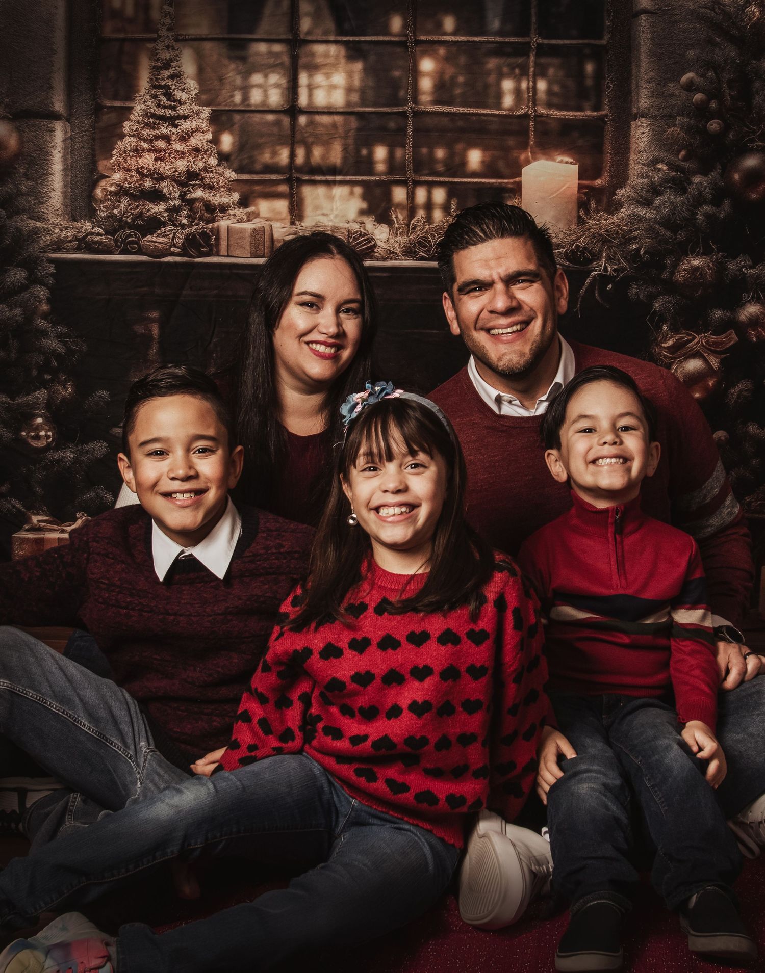 A series of warm-toned family portraits featuring coordinated outfits in red and burgundy tones against a dark background.