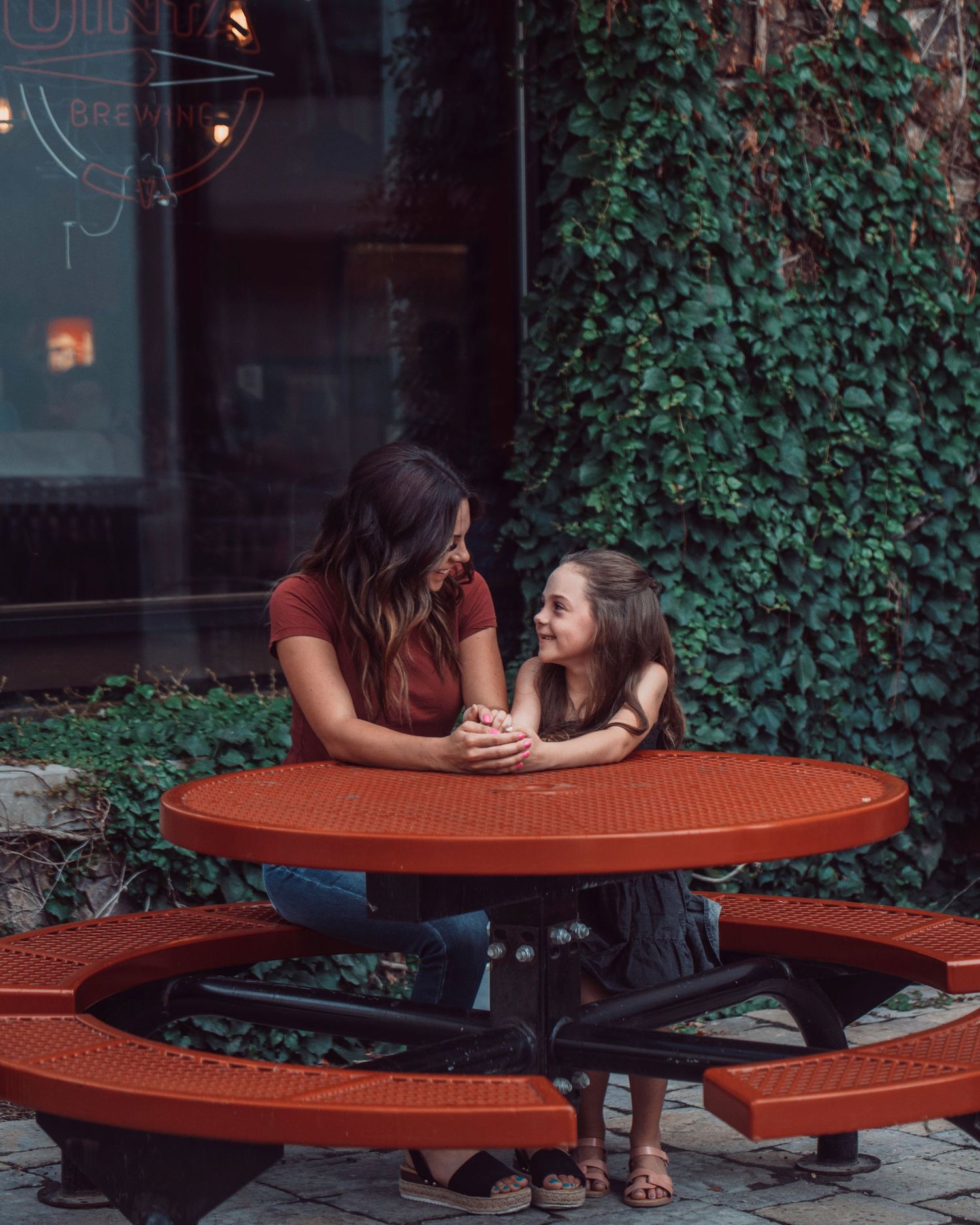 A couple sits together on a curved red outdoor bench surrounded by ivy-covered walls.