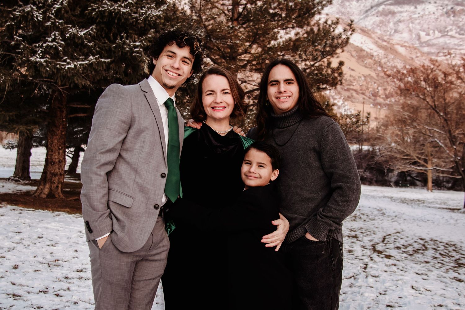 A family poses together in a snowy winter setting wearing coordinated dark and neutral colored outfits.