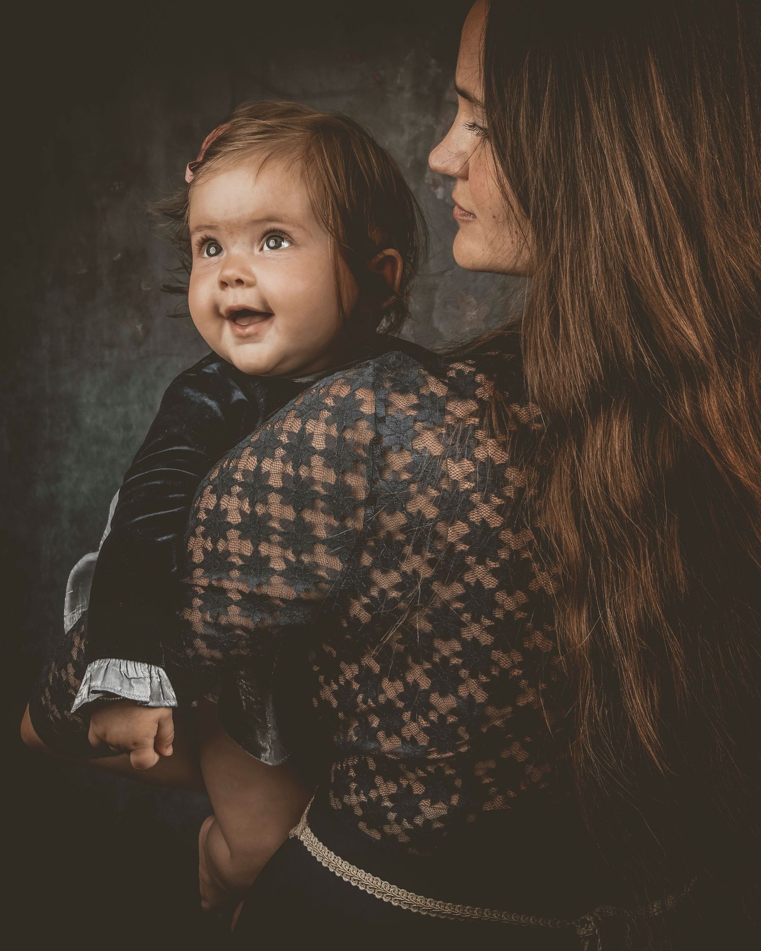 A heartwarming series of candid moments between parent and baby captured in moody, artistic lighting against a dark backdrop.