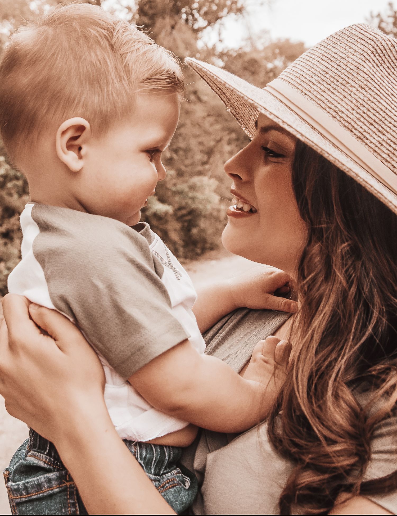 A tender moment between parent and child in warm sunlight, with the adult wearing a sun hat.
