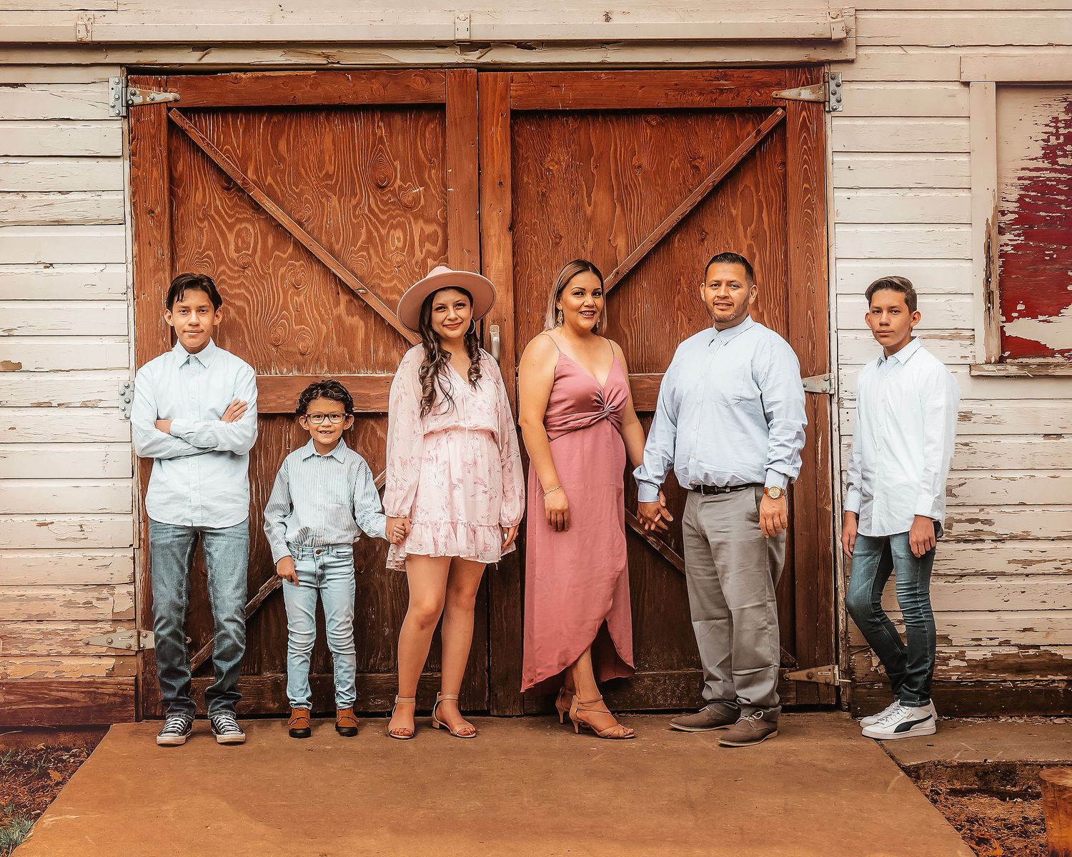 A rustic family photo session against a white wooden barn with brown doors creating a vintage farmhouse aesthetic.