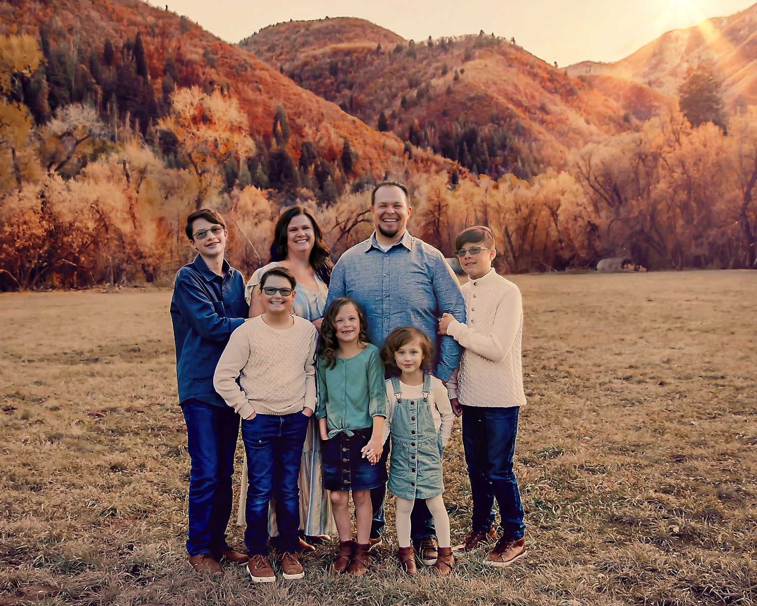 A series of outdoor family portraits captured at sunset in a golden meadow with mountains in the background.