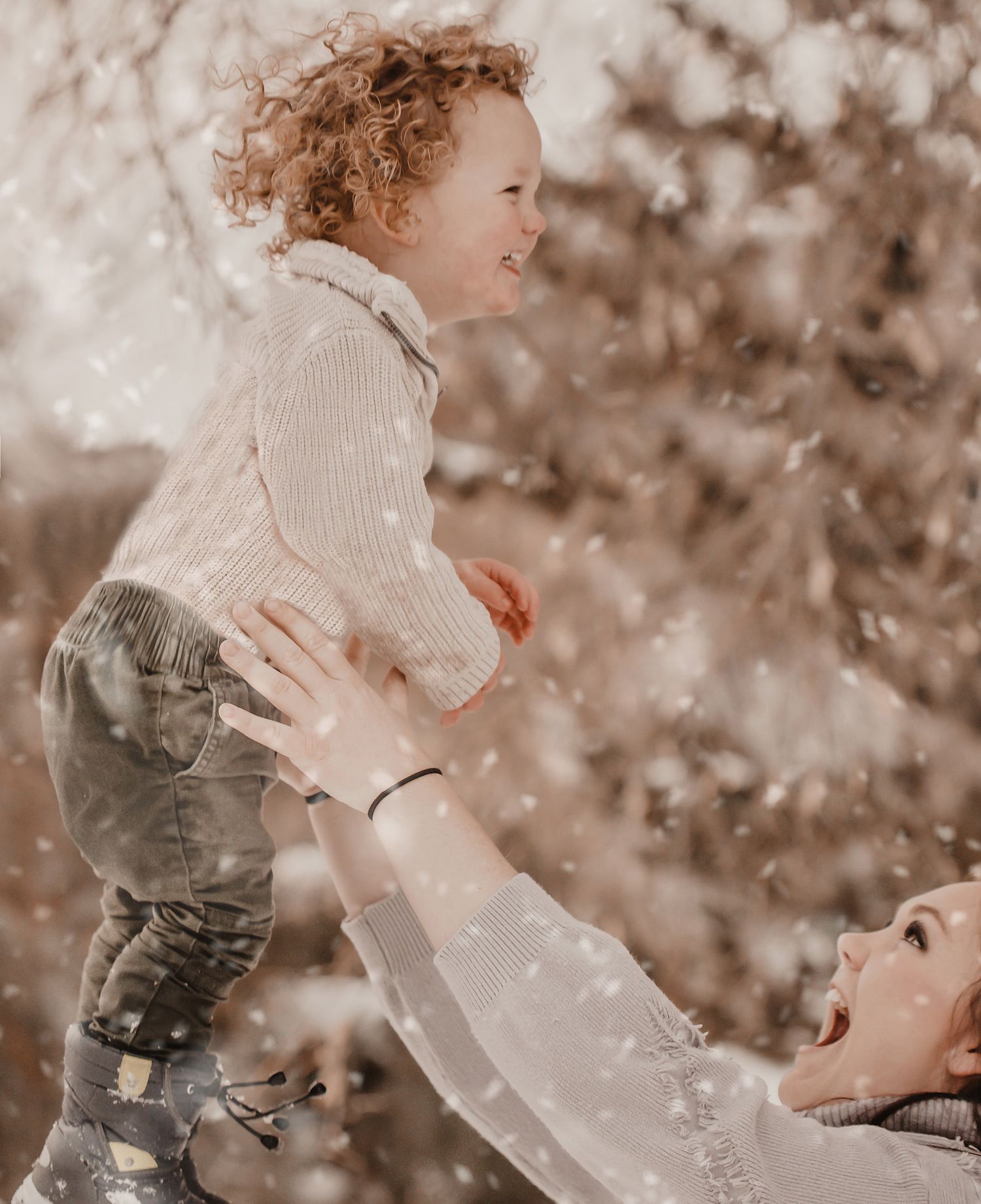A joyful moment captured in sepia tones as a child is lifted playfully into the air during a snowy winter day.