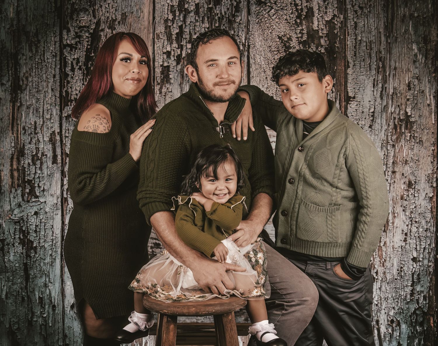 Family portrait session against a rustic dark wooden wall backdrop with moody lighting.
