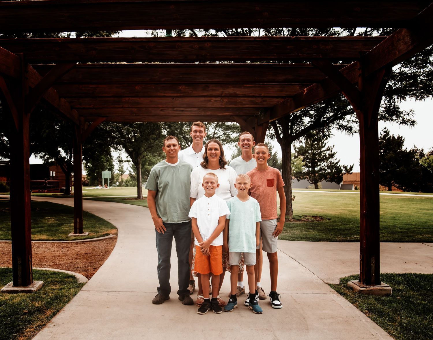A group of people walking together on a paved path through a park on a sunny summer day.