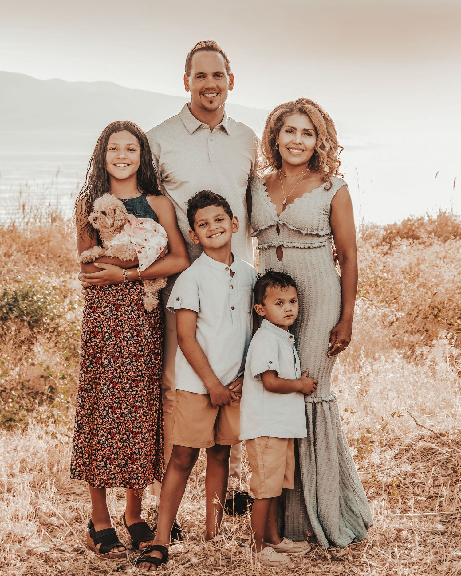 A warm-toned outdoor family portrait series in a field with neutral earth-tone clothing and natural lighting.