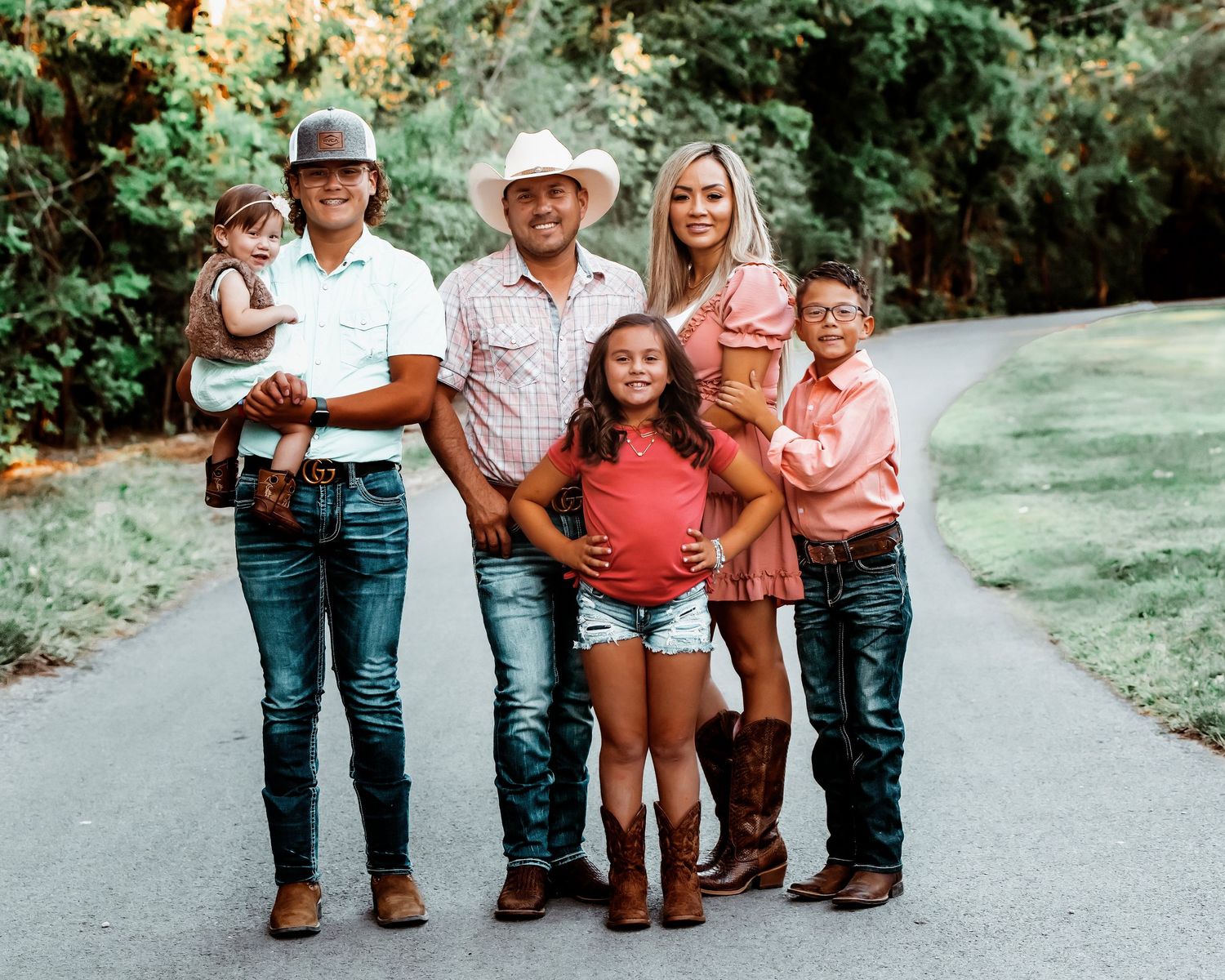 A group of people wearing cowboy boots and casual clothing stand together on a gravel path in an outdoor setting.