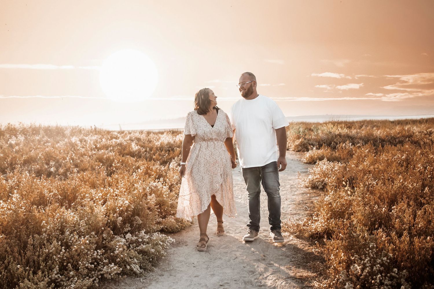 A couple walks hand in hand through a golden field at sunset creating a romantic silhouette against the warm sky.