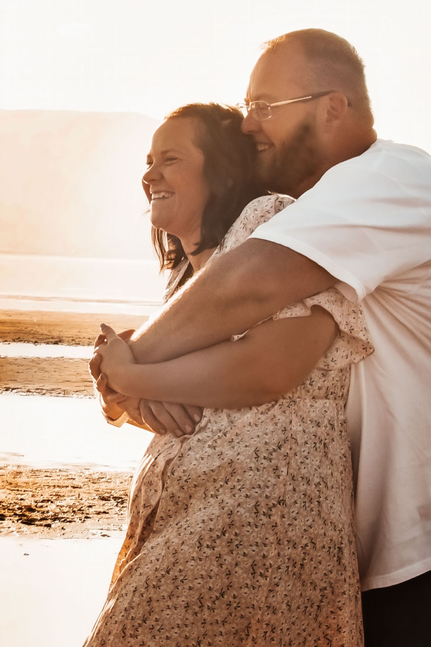 A couple embraces on a beach at sunset, creating a romantic silhouette against the golden light.