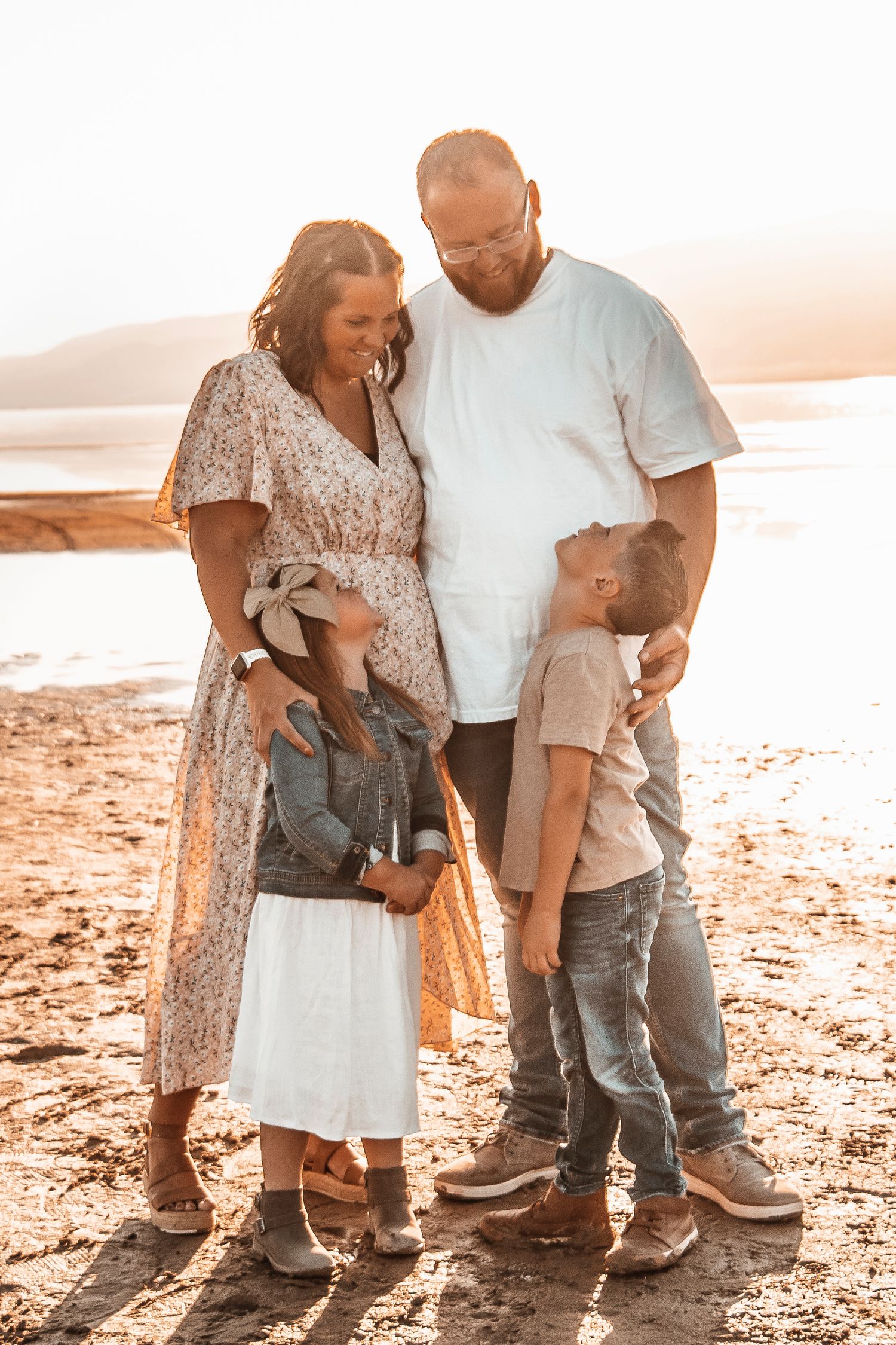 Family in casual attire stands together on a sandy beach at sunset creating warm, intimate moments.