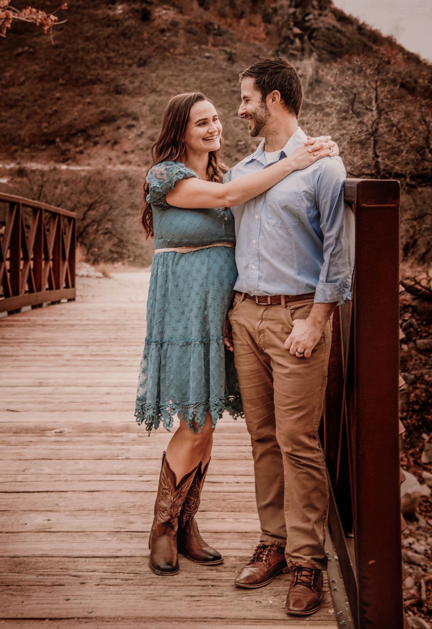 A romantic couple shares a tender moment on a wooden boardwalk wearing rustic western attire in sepia tones.