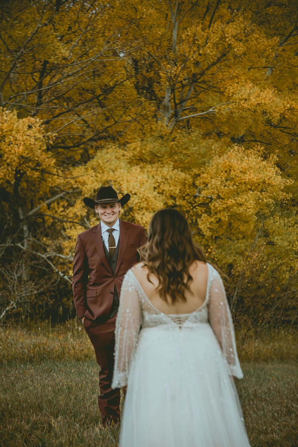 A romantic autumn scene with a couple amid golden foliage, bride in white gown and groom in burgundy suit. Saskatchewan Wedding Photographer