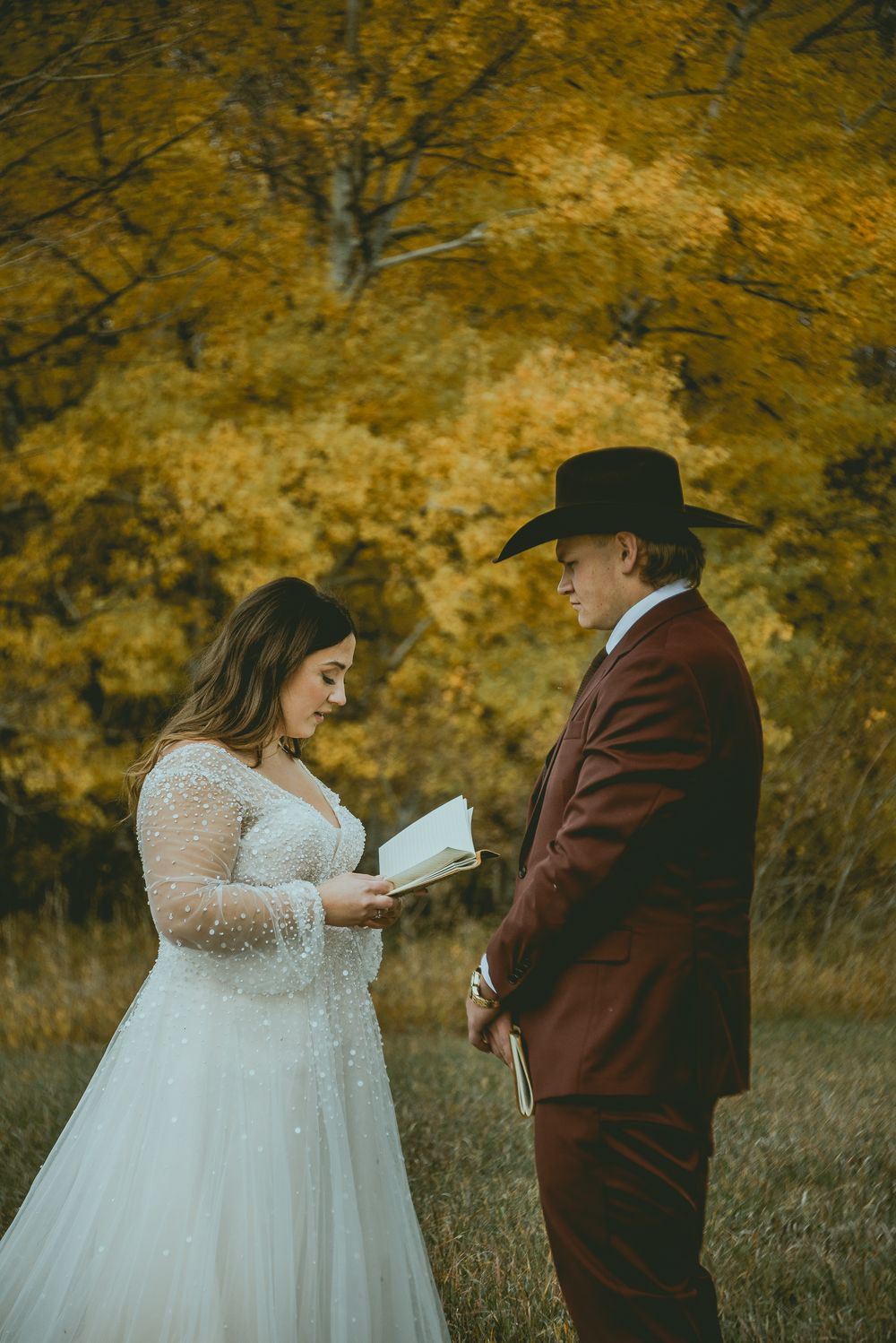 Wedding couple shares an intimate moment reading from a book against a backdrop of vibrant fall foliage. Saskatchewan Wedding Photographer