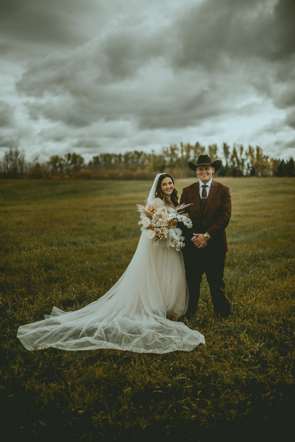Wedding couple poses in a dramatic field under stormy skies during fall season. Saskatchewan Wedding Photographer
