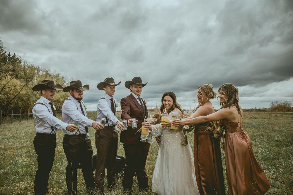 Wedding party members enjoy a playful moment in an outdoor field under dramatic cloudy skies. Saskatchewan Wedding Photographer