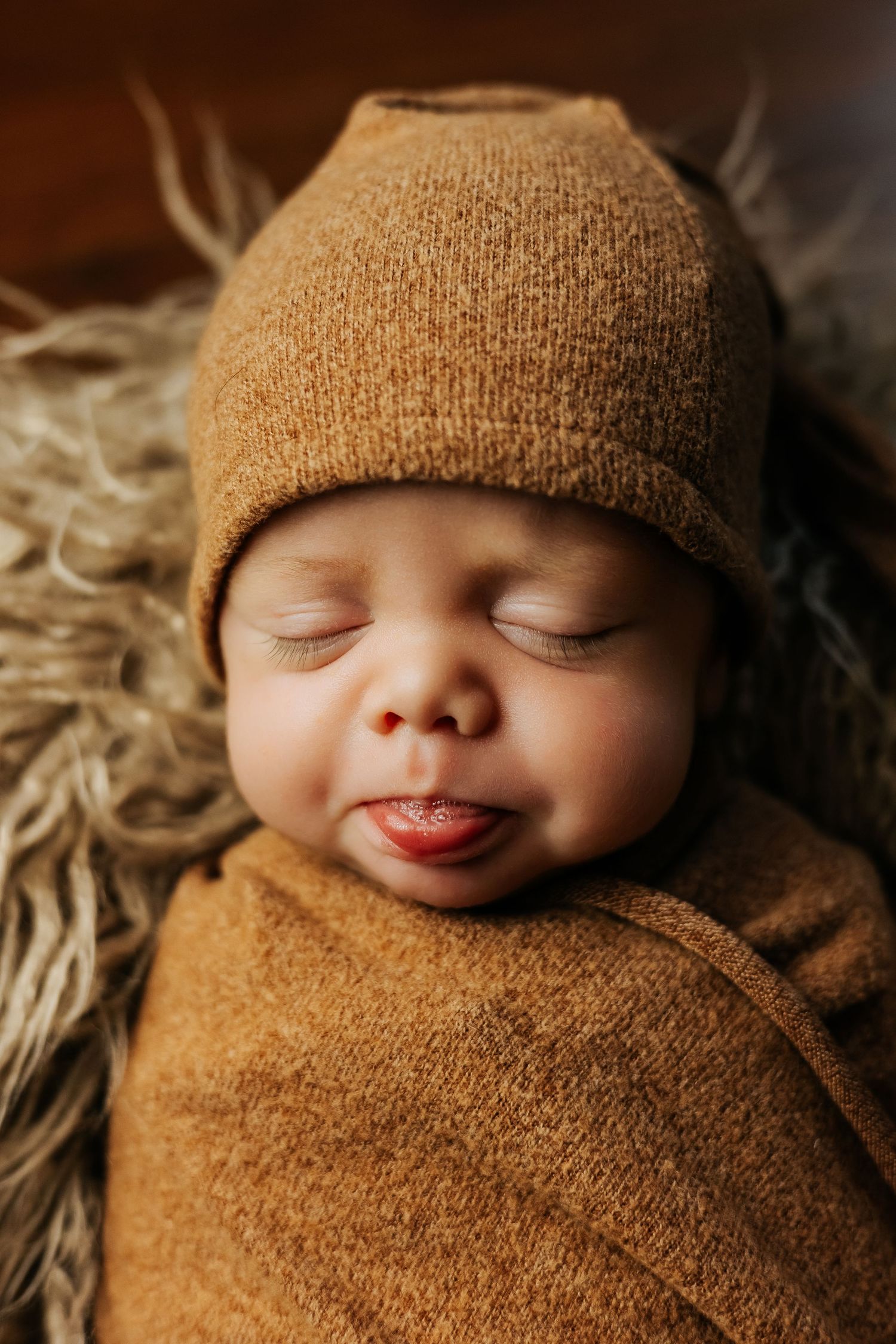 Peaceful newborn wrapped in brown knit blanket with matching beanie.