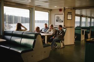 Passengers relax in comfortable seating aboard a ferry with large windows offering scenic water views.