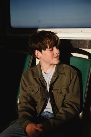 Person in brown jacket sits in green car seat against dark background with dramatic lighting and shadows.