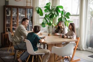 People sit at a table in a bright, modern dining room with large windows and potted plants.