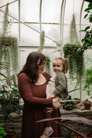 A tender moment between two people in a greenhouse filled with plants and natural light.