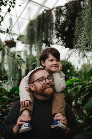 A couple shares tender moments together in a greenhouse surrounded by lush greenery and hanging plants.