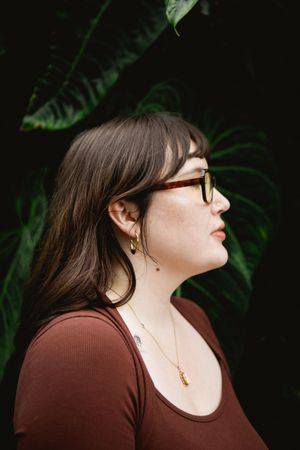Profile view of someone wearing a brown top against lush green foliage in dramatic lighting.