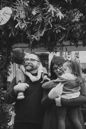 Black and white photos capturing tender embraces between a bearded person in glasses and a small child against foliage.