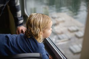 Child looking thoughtfully out of a window while sitting in a car seat during a journey.
