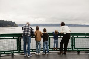 People stand at a railing overlooking a scenic waterfront view on an overcast day.