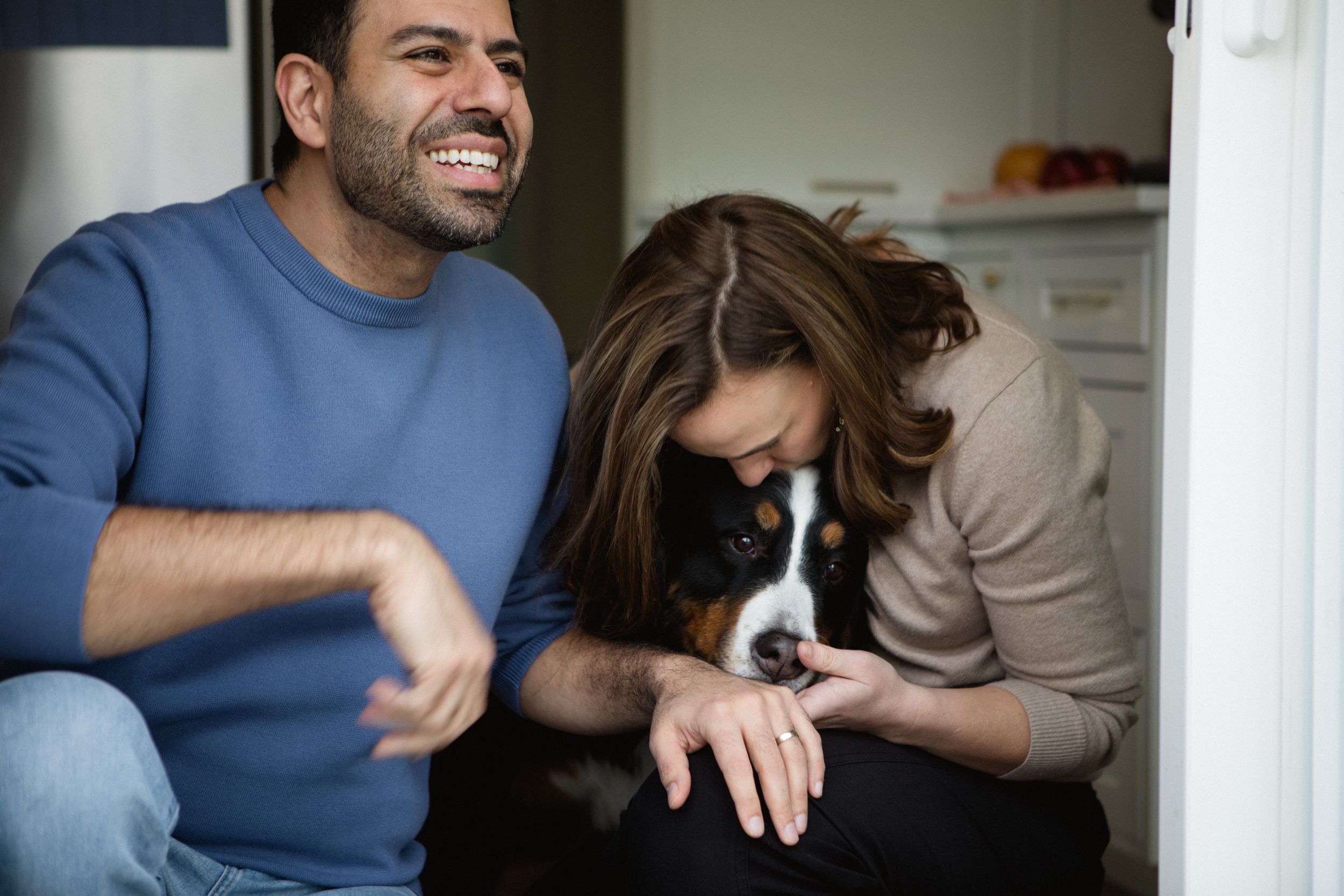 A couple sits on a couch together playing and cuddling with their small black and white puppy.